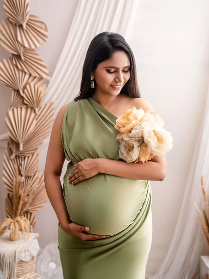 A close-up portrait focusing on the beautiful mom-to-be. The soft green dress, bouquet of peonies, and natural backdrop create a serene and earthy vibe.