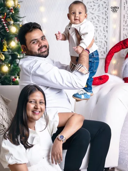 A beautiful family portrait, with the father holding up their little one, all sharing smiles in our cozy Christmas corner.