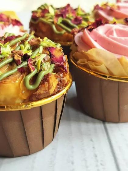 A side view of the Baklava cupcakes, showing the beautiful golden-brown cupcake liners and the generous toppings. The pink rose-flavored buttercream provides a lovely contrast to the pistachio.