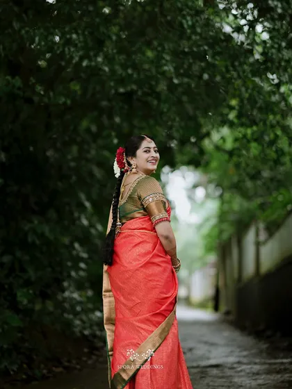 The bride looking back with a joyful smile, her traditional red saree and braided hair creating a timeless look.