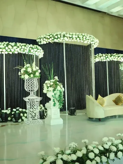 A minimalist yet striking reception stage. The backdrop of clean white panels and a dark, beaded curtain is accented by clouds of white flowers, creating a modern and elegant look.