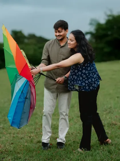 A fun and colourful pre-wedding photo, where a couple plays with a rainbow umbrella in a green meadow, symbolizing the joy and brightness of their love.