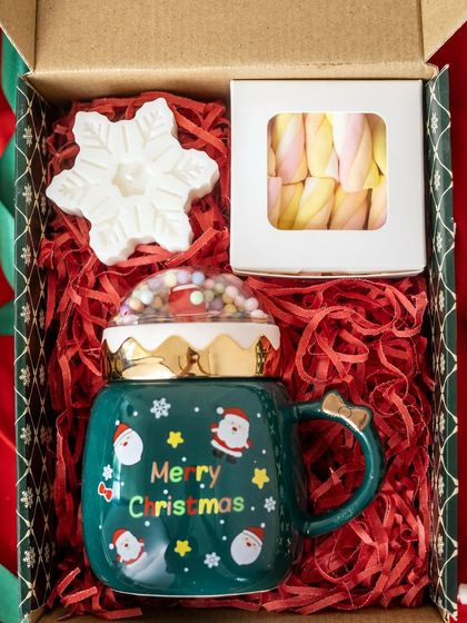 This festive hamper is perfect for a cozy Christmas morning. It features a "Merry Christmas" mug with a cute lid, a snowflake candle, and a box of marshmallows.