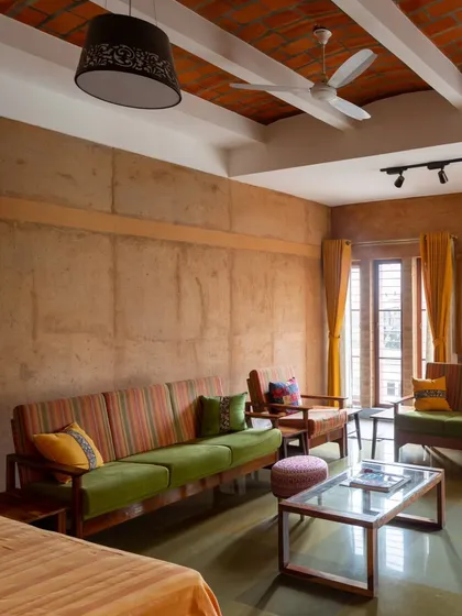 The living room in Radhika and Manoj's residence features a prominent wall made of rammed earth from the site. Paired with simple furniture and natural light, it creates a warm, inviting atmosphere that is both rustic and modern.
