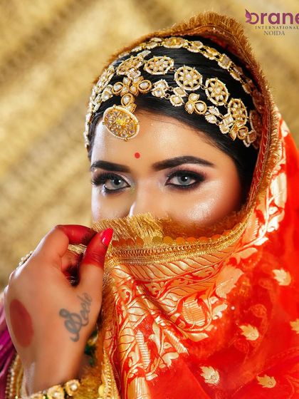 A classic bridal pose, with the veil partially covering the face, drawing attention to the expressive eyes and intricate matha patti.