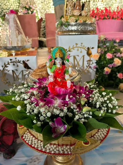 A small Lakshmi idol placed in a decorated bowl with flowers, bringing blessings to the event.
