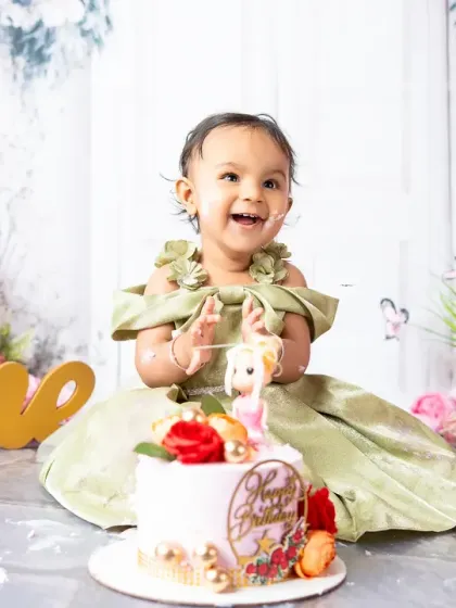Pure happiness captured during a first birthday cake smash session. Dressed in a beautiful gown amidst a floral setup, this little one's joyful expression is what these celebratory milestone photoshoots are all about.