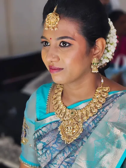 A simple and elegant look for this bride. The focus is on clean skin, neatly defined eyes, and traditional gold jewelry against a beautiful blue silk saree.