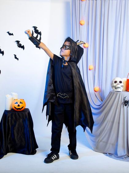 A child in a bat-themed costume with a cape and mask, posing heroically.