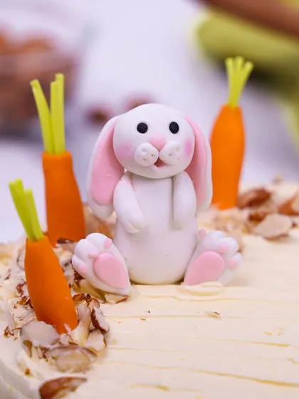 A close-up of the adorable, hand-crafted bunny topper, nestled among fondant carrots and nuts.