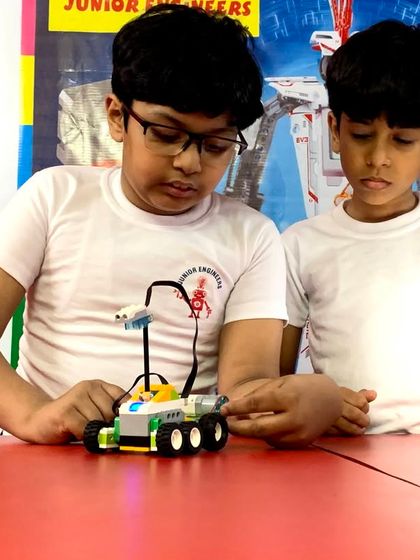 Two boys work intently on their wheeled robot, making adjustments to its sensor. This image captures the focus and hands-on problem-solving that our robotics sessions foster.