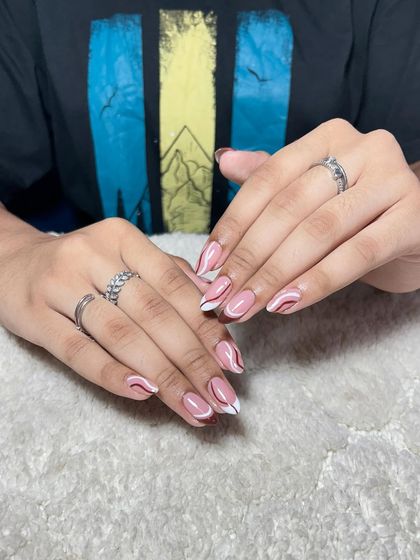 A playful design with a nude base and abstract swirls of white and red on almond-shaped nails.