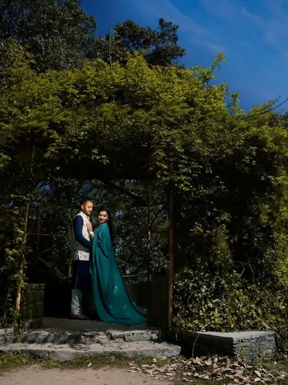 A wide shot of a couple standing under a natural archway of lush green foliage. This image shows how I use natural frames within the landscape to create depth and focus in a pre-wedding photograph.