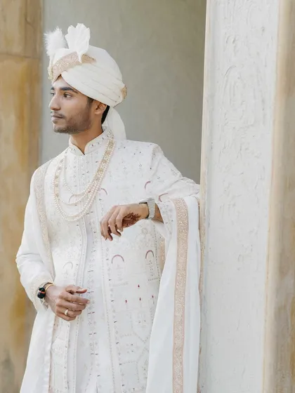 An elegant portrait of the groom, Sanket. His pristine white sherwani and the simple, clean background create a timeless and regal image.
