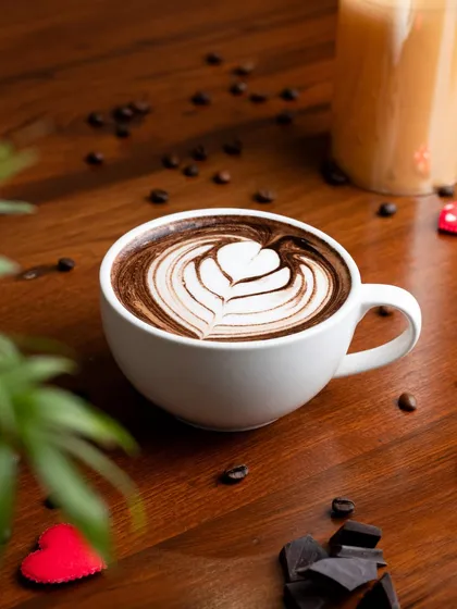 A beautiful mocha with heart-shaped latte art, styled with chocolate and coffee beans. A perfect image for a cafe's Valentine's Day promotion.