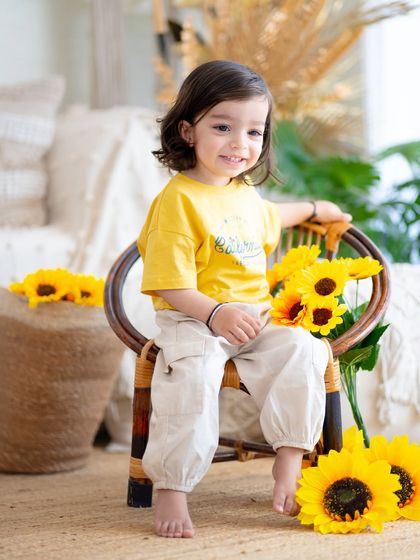 A bright and sunny portrait with sunflowers. This little one's happy smile is as bright as the flowers beside her.