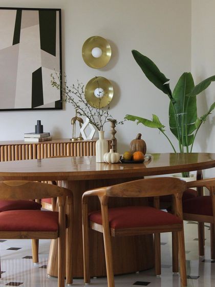 A close-up of the dining area, where warm wood furniture with red upholstery is set against a backdrop of abstract art and brass wall sconces. The space feels both vibrant and grounded.