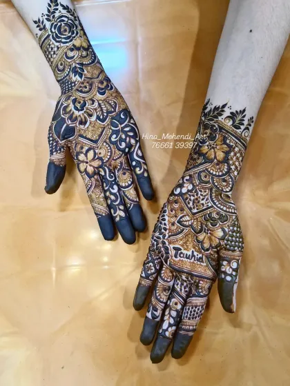 The beautiful contrast of a dark henna stain. The design features bold flowers and the name 'Tauhid' on the palm.