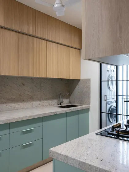 This view showcases the beautiful contrast between the cool mint green cabinets, the warm fluted wood, and the textured quartz countertop. The glass partition offers a glimpse into the utility area, showing how every part of the home is connected.