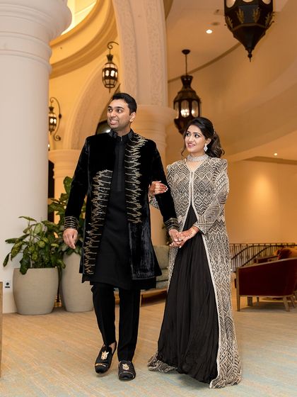Walking hand-in-hand, the couple makes a grand entrance at their reception. Their coordinated black and silver outfits are the epitome of evening glamour.