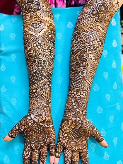 A stunning bridal design on both hands, set against a bright blue background that makes the henna pop.