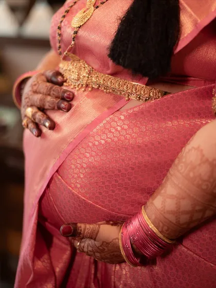 This detail-oriented shot focuses on the mother-to-be's hands, decorated with henna, cradling her baby bump. The vibrant pink saree and traditional gold jewelry highlight the cultural beauty of the ceremony.