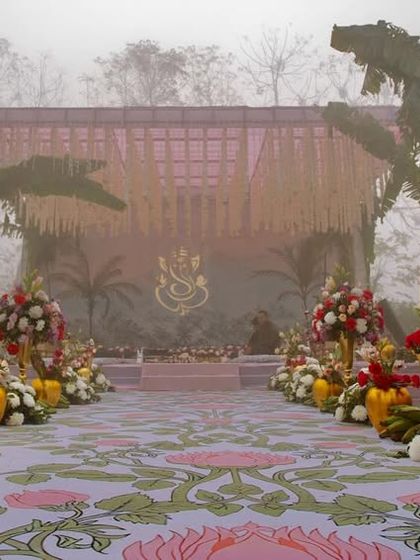 The main aisle leading to the mandap, with a custom-printed floral runner and flanked by large banana leaf arrangements in golden vases.