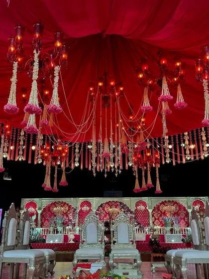 This mandap features a dramatic red draped ceiling from which hang floral-adorned chandeliers and strings of jasmine, creating a rich and romantic atmosphere.
