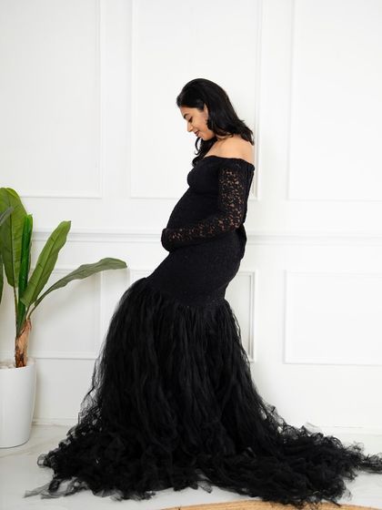A quiet moment of reflection. This full-length shot of a mom-to-be in a black lace mermaid gown emphasizes her silhouette against a clean, minimalist white background.