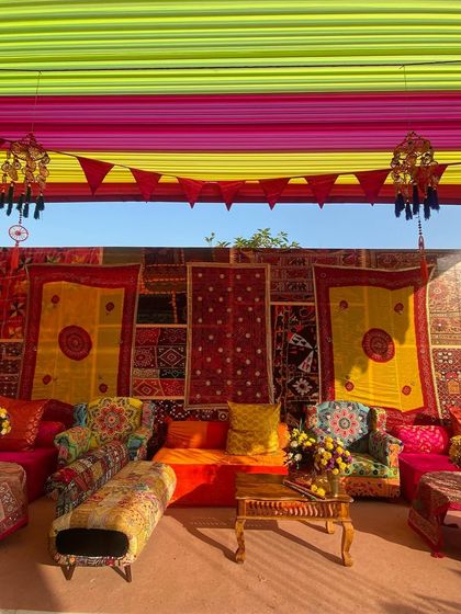 A comfortable lounge area from the Kathiyawadi Haldi, featuring colorful patchwork sofas and a backdrop of traditional embroidered textiles. The decor is a rich tapestry of color and culture.