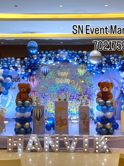 A grand teddy bear themed stage in blue, white, and silver. The setup includes a sequin backdrop, teddy bears on balloon pillars, and light-up letters spelling the name 'Hanvik'.