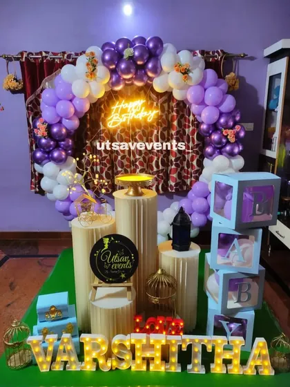 A purple and white ring-themed decor for a birthday. This setup includes a balloon arch, neon sign, and transparent 'ABC' blocks.