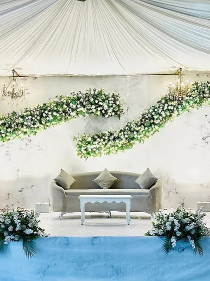 This elegant stage design features a marble-textured backdrop with two graceful swags of greenery and white flowers. The minimalist furniture and classic chandeliers complete the sophisticated look.