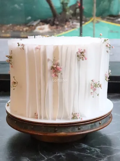 This minimal cake with wafer paper draping and pink baby's breath sits beautifully on a rustic wooden stand.