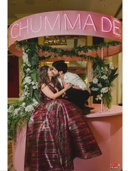 The couple shares a kiss at their custom 'Chumma De' bar. These playful, personalized elements make for unforgettable photos and memories.