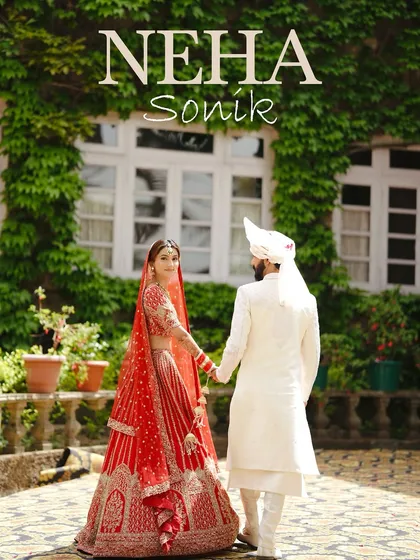 A bride in a stunning red lehenga leads her groom, dressed in elegant white, through the ivy-covered courtyard of a heritage palace. This classic wedding portrait captures the timeless grace and grandeur of the wedding day.