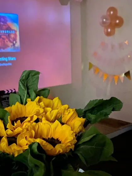 A simple yet beautiful gesture with a bouquet of sunflowers set against the backdrop of the projector screen and birthday banners.