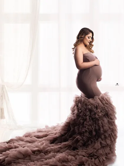 A classic profile shot against a bright window, highlighting the beautiful silhouette of the client in a dusty mauve ruffled gown. This is a timeless and elegant maternity portrait.