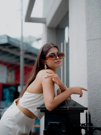 A stylish portrait of a model leaning against a post on the street. Her all-white outfit and sunglasses create a chic and sophisticated urban look.