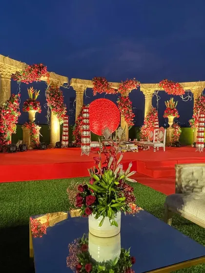 The 'Jashn e Ishq' themed mandap at dusk. The dramatic lighting enhances the rich red color palette and the grandeur of the Roman-inspired pillars, creating a truly cinematic setting.