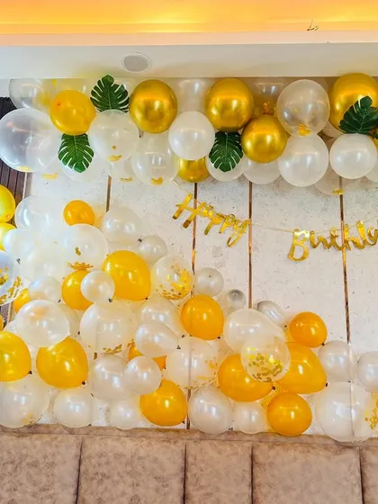 A classy birthday decoration over a bed, with a cascade of white, clear, and gold balloons.