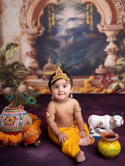Our little Kanha sitting proudly with his pot of butter, peacock feathers, and a friendly cow statue. I provide all the props for these detailed setups.
