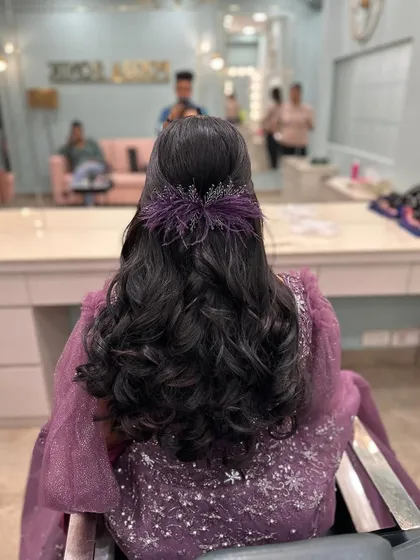 A half-pinup hairstyle with curls, finished with a unique purple feather and crystal accessory.