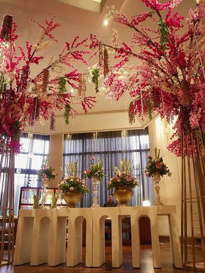 A stunning ceiling installation of pink cherry blossoms and hanging glass globes creates a magical, forest-like canopy over the reception entrance area.