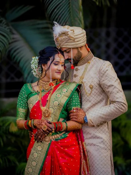 A stunning portrait of a traditionally dressed Maharashtrian couple. The bride's green and red saree and gold jewelry are perfectly complemented by the groom's elegant attire.