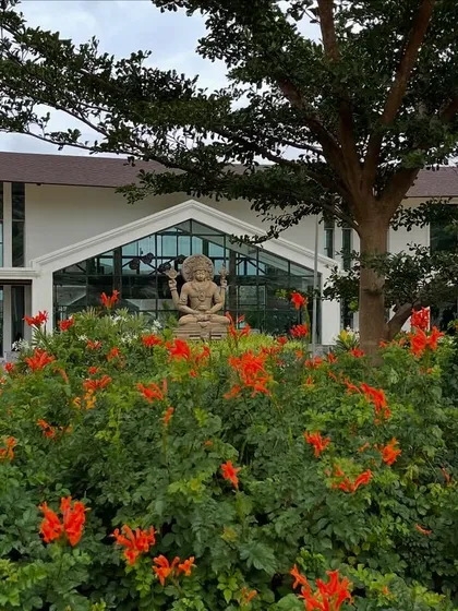 The vibrant orange flowers blooming in our garden, with the main building and Dhanvantari statue in the background. The summer season brings a joyful burst of color to the retreat.