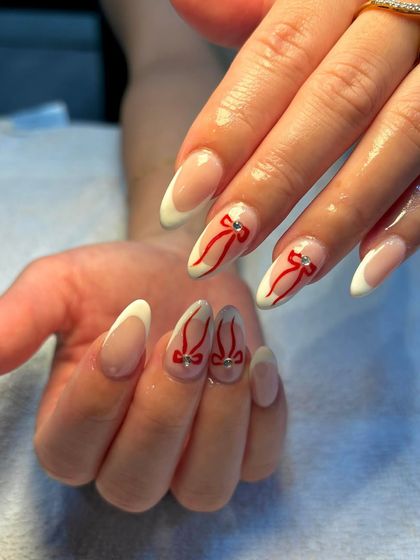 Sweet, chic, and wrapped with a bow. This adorable design features a classic French manicure base with accent nails decorated with hand-painted red ribbons and a tiny rhinestone.