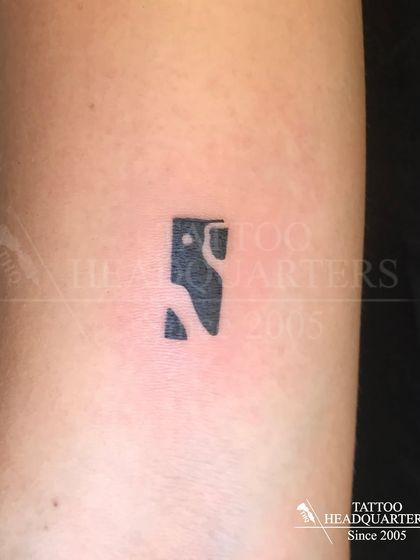 A minimalist negative space tattoo, where the shape of a person is formed by the un-inked skin within a black rectangle.