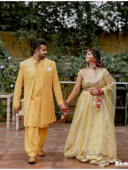 A romantic walking shot of the couple after their Haldi ceremony. Dressed in coordinated yellow outfits, they hold hands and share a loving glance, capturing a quiet moment amidst the celebrations.
