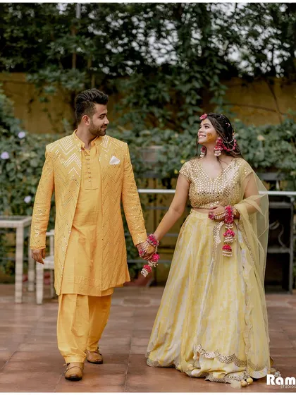 A romantic walking shot of the couple after their Haldi ceremony. Dressed in coordinated yellow outfits, they hold hands and share a loving glance, capturing a quiet moment amidst the celebrations.